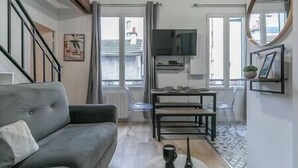 Una sala de estar con un sofá gris, una mesita, un televisor y una ventana con cortinas.