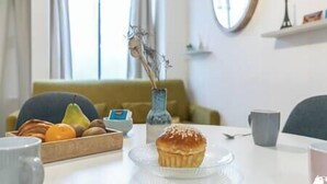 Une table à manger avec un muffin, un panier de fruits et un vase contenant des fleurs séchées.