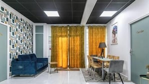 A living room with a blue sofa, a dining table with chairs, and a yellow curtain.