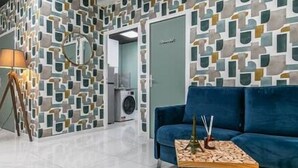 A modern room with a geometric patterned wall, a blue sofa, a lamp, and a small table with decorative items.