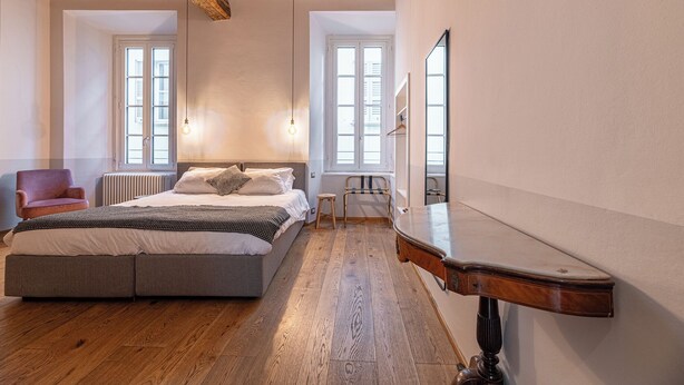 A bedroom with a bed, a chair, a radiator, and a wooden ceiling. - Guesthouse Volta38 in the center of Como! (Como)