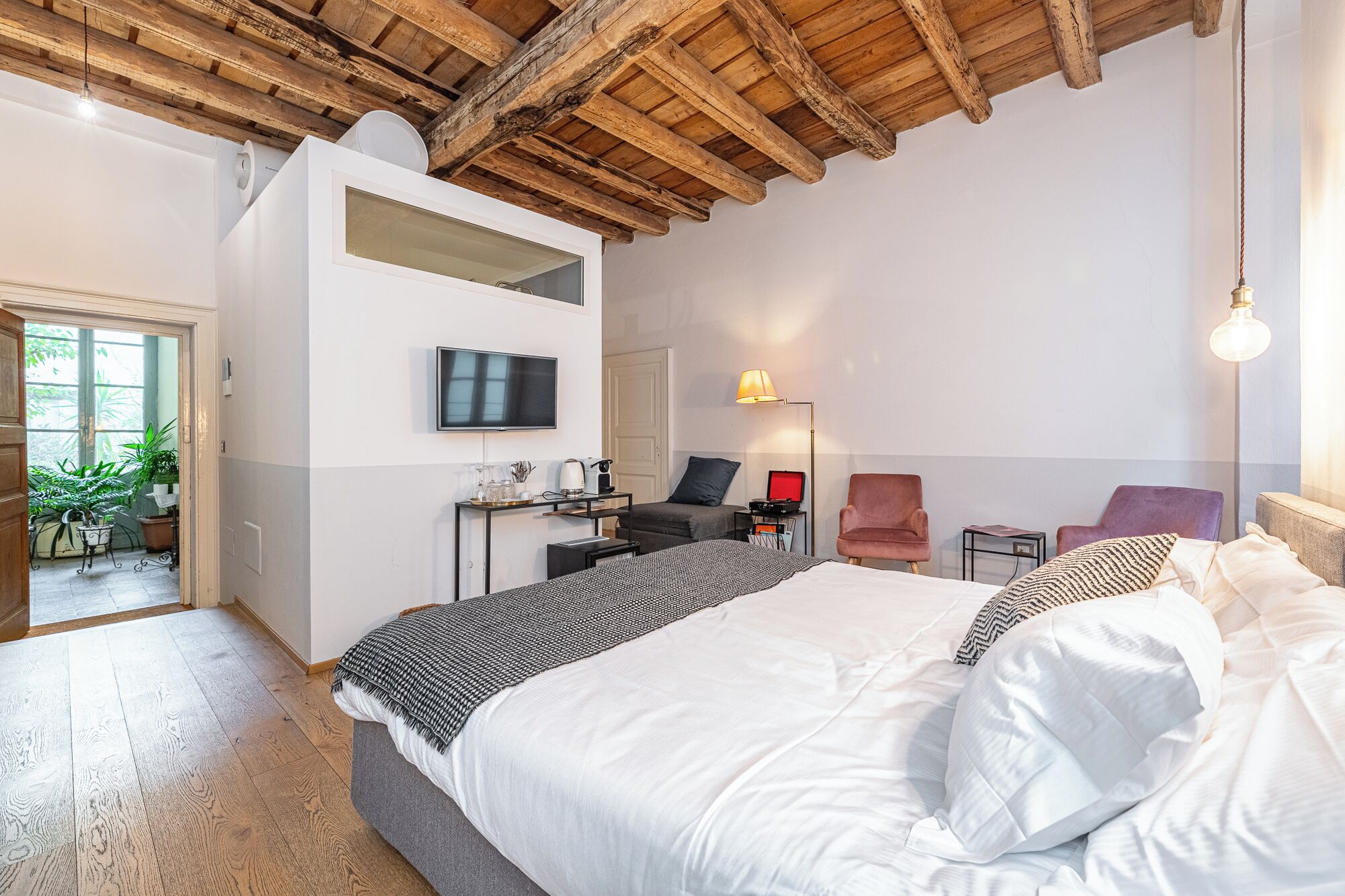 Ein modernes Schlafzimmer mit einem großen Bett, einem Schreibtisch, einem Stuhl, einem Fernseher und einer Decke mit freiliegenden Balken.