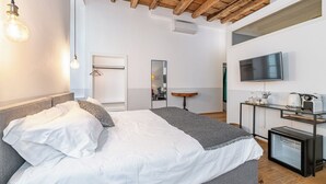 A modern bedroom with a wooden ceiling, a bed with white linens, a bedside table with a mirror, a TV, and a small kitchenette. - Guesthouse Volta38 in the center of Como! (Como)