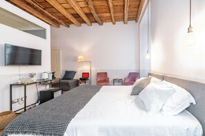 A hotel room with a bed, a desk, a chair, a TV, and a lamp.
