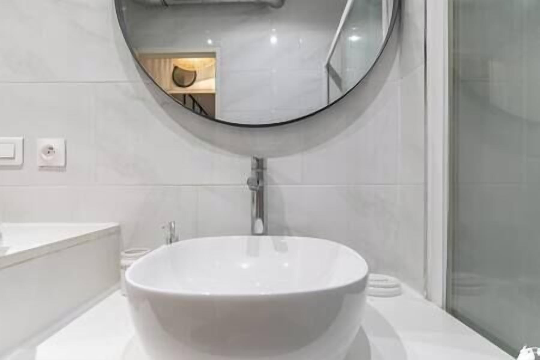 Een badkamer met een ronde spiegel, een wit wastafelmeubel en een douchecabine van glas.