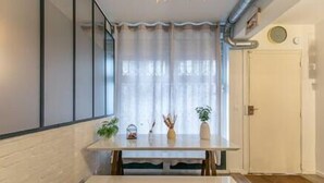 A small, modern kitchen with a white countertop, a window with sheer curtains, and a door with a round light fixture.
