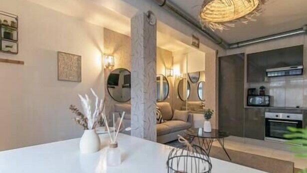 A modern living room with a white dining table, a sofa, and a kitchen area with a microwave.
