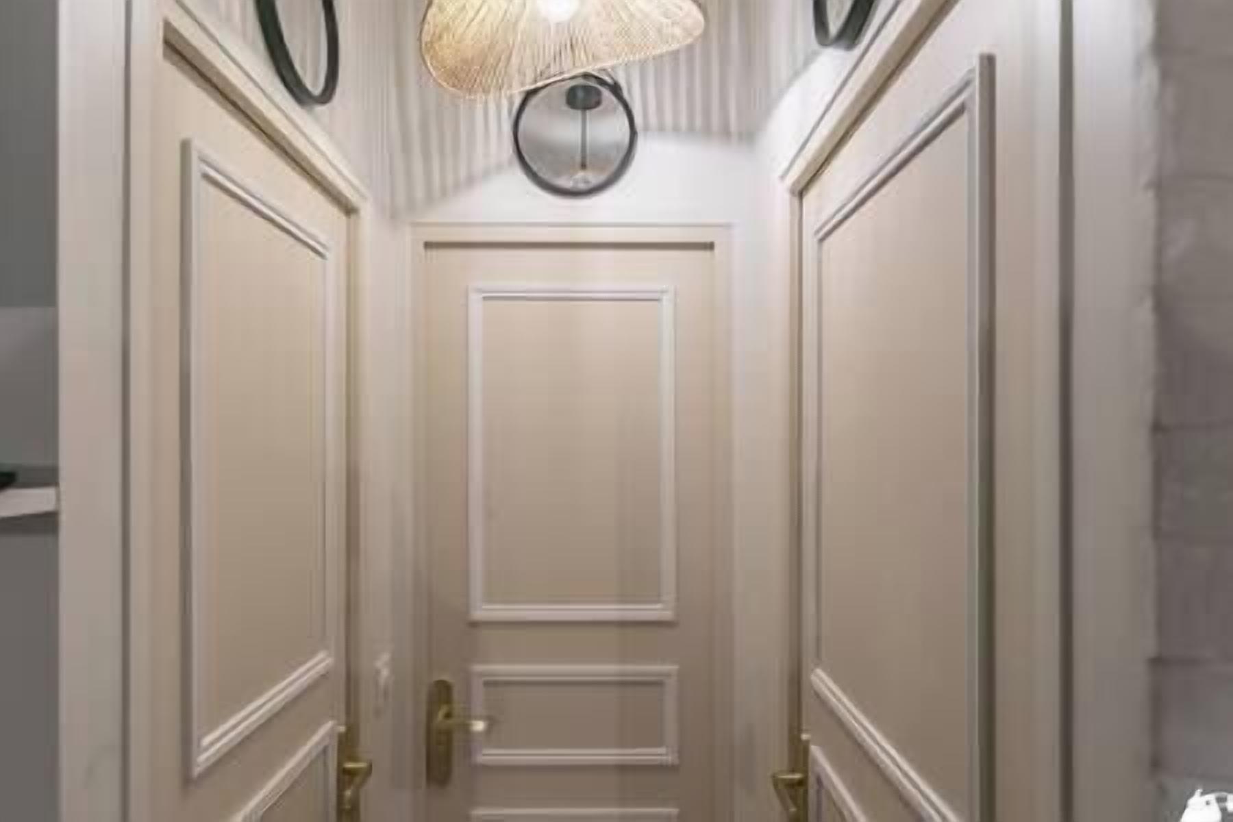 A hallway with a closed door, a textured ceiling light fixture, and a wall-mounted round clock.