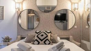 A modern hotel room with a large bed, three wall-mounted mirrors, and a decorative pillow.