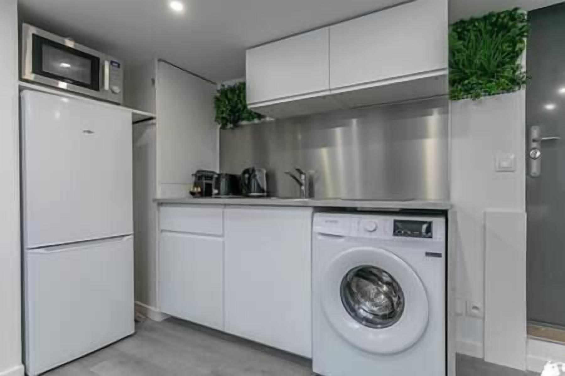 Een compacte keuken met een ingebouwde wasmachine en droger, een magnetron en een koffiezetapparaat.