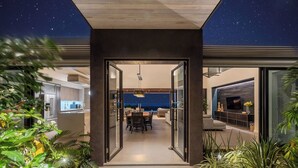 A modern house with a glass door leading to a dining area and a living room with a TV.