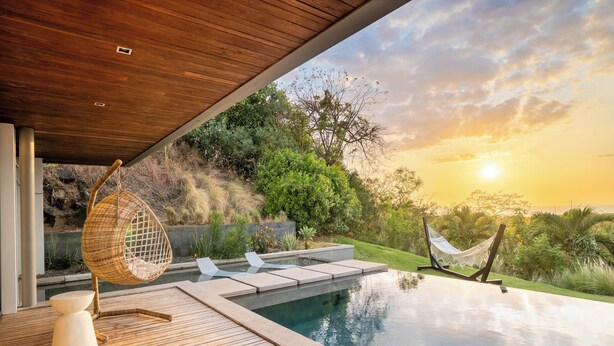 A modern outdoor pool area with a wooden deck, lounge chairs, and a hammock.