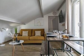 A cozy living room with a sofa, a dining table set for two, and a large window. - MBA Splendide Appart -Montreuil 2-Proche Vincennes (Montreuil)