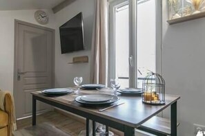 A dining area with a table set for four, a television on the wall, and a window with curtains. - MBA Splendide Appart -Montreuil 2-Proche Vincennes (Montreuil)