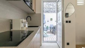 A modern kitchen with a built-in stove, a coffee machine, and a glass door leading to an outdoor seating area. - MBA - Felix Faure Luxury Appart proche Tour Eiffel (Paris)