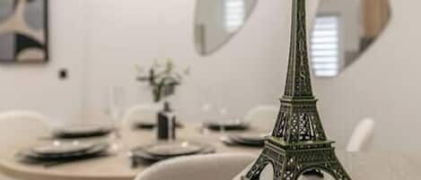 A dining table with a model of the Eiffel Tower, a vase with flowers, and a painting on the wall.