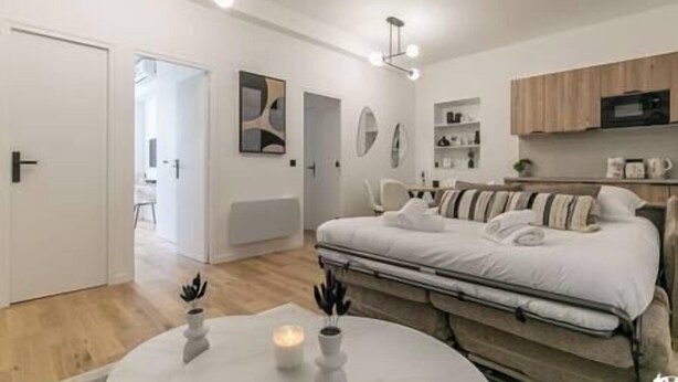 A modern bedroom with a bed, bedside tables, a small table with candles, and a view of a hallway. - MBA - Felix Faure Luxury Appart proche Tour Eiffel (Paris)