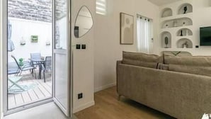 A living room with a sofa, a TV, and a glass door leading to an outdoor area with a table and chairs. - MBA - Felix Faure Luxury Appart proche Tour Eiffel (Paris)