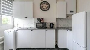 A modern kitchen with white cabinets, a microwave, a kettle, and a clock on the wall. - MBA - Splendide Appart Proche Château Vincennes (Vincennes)