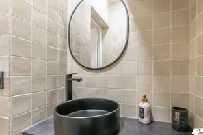 A bathroom with a round sink, a mirror, and a bottle of hand soap.