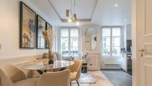 Un espace repas moderne avec une table ronde en verre, des chaises de couleur beige et un vase contenant des fleurs séchées.