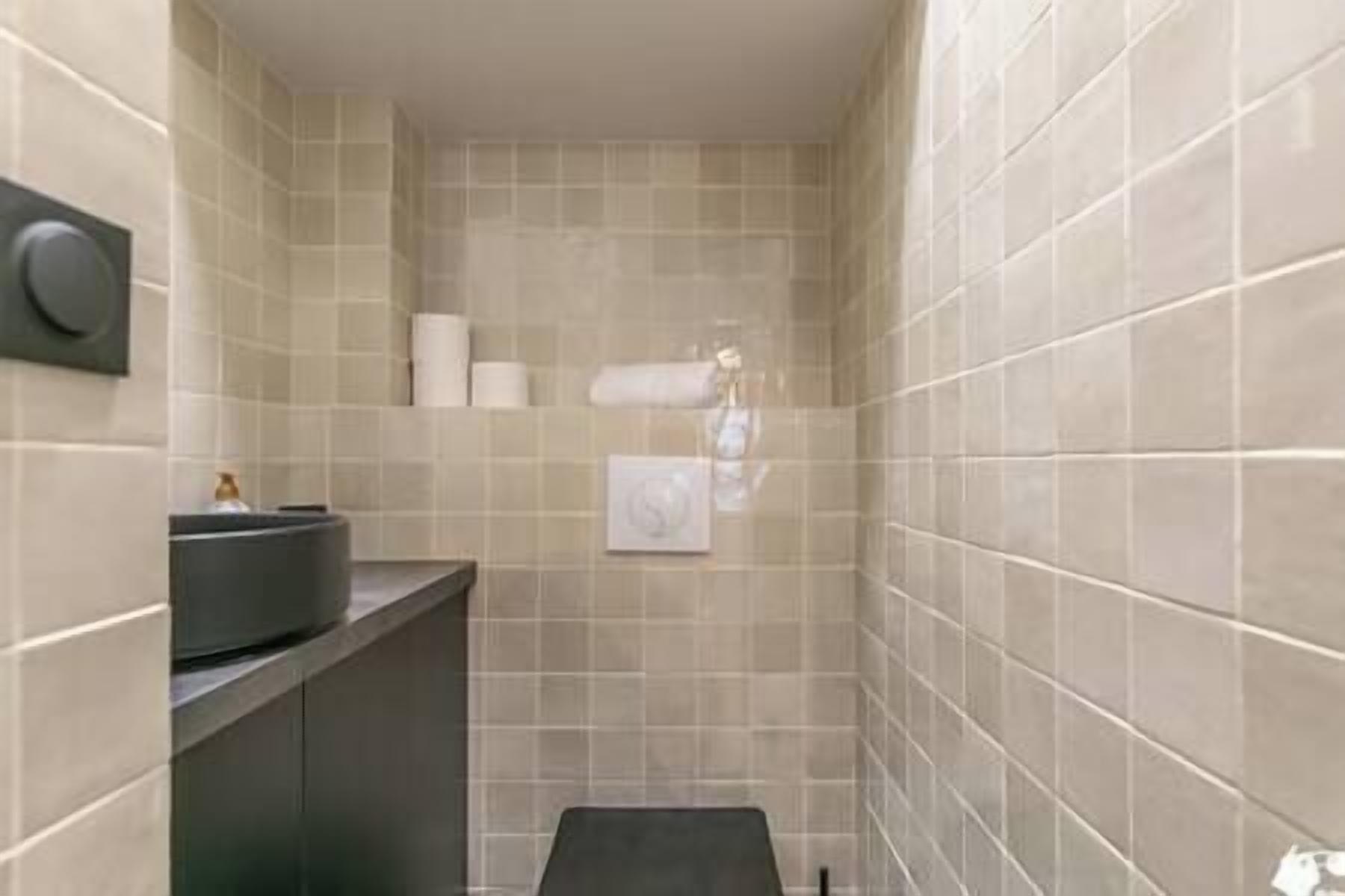 Een kleine badkamer met beige tegels, een zwarte wastafel en een toilet.