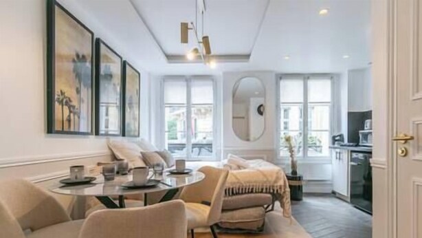 Un salon moderne avec un canapé, une table à manger et un coin cuisine visible à travers une porte ouverte.