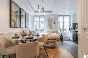 Un salon moderne avec un canapé, une table à manger et un coin cuisine visible à travers une porte ouverte.