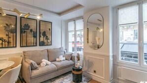 Un salon moderne avec un canapé beige, un miroir rond et des œuvres d’art accrochées au mur.