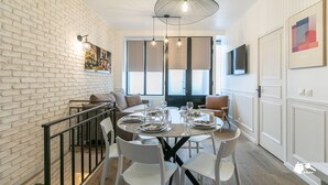 A dining area with a brick wall, a round table set for four, and a modern pendant light. - MBA - Cavalloti Splendide Appartement (Paris)