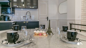 A modern kitchen with dark cabinets, a white tiled backsplash, and a marble countertop. There are two black mugs, a glass, and a small Eiffel Tower model on the table. - MBA - Cavalloti Splendide Appartement (Paris)