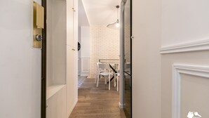 A hallway with white walls, a wooden floor, and a dining area with a brick wall and white furniture. - MBA - Cavalloti Splendide Appartement (Paris)