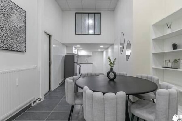 A modern dining area with a round table, grey upholstered chairs, and a vase with flowers.