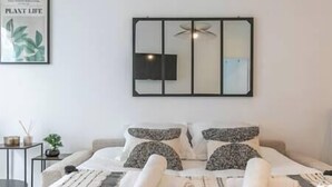 A modern bedroom with a bed, pillows, a bedside table, a small plant, and a framed picture on the wall.
