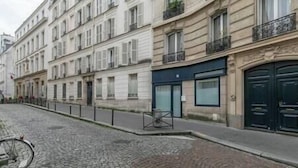 A street view with a building featuring a black door and a storefront with a blue awning.