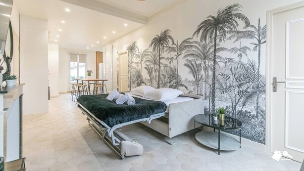 Une chambre d’hôtel moderne avec un lit, un coin repas et une fresque murale aux motifs tropicaux.