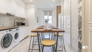 Une cuisine moderne dotée d’une table à manger centrale, d’appareils électroménagers intégrés et offrant une vue sur l’extérieur.