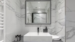 Une salle de bain moderne avec un grand lavabo rectangulaire, un miroir au-dessus et des murs en marbre.