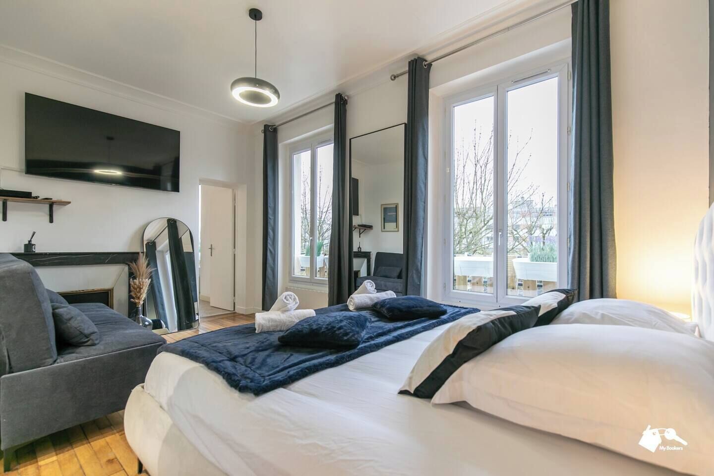 Ein modernes Schlafzimmer mit einem großen Bett, einer Couch, einem Fernseher und einem Fenster mit Vorhängen.