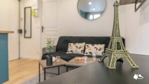 Una maqueta de la Torre Eiffel sobre una mesa en una habitación con un sofá negro, un espejo redondo en la pared y una puerta al fondo.