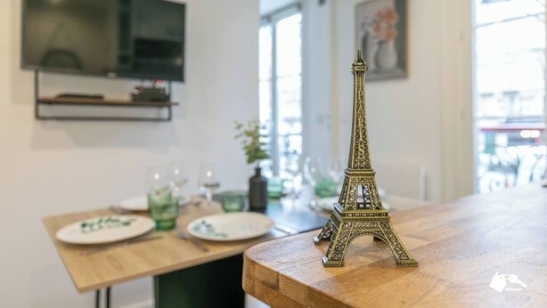 Un área de comedor con una mesa de madera, un pequeño modelo de la Torre Eiffel y un televisor montado en la pared.