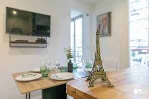 Un área de comedor con una mesa de madera, un pequeño modelo de la Torre Eiffel y un televisor montado en la pared.
