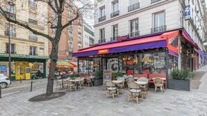 Un café al aire libre con sillas y mesas de mimbre, un toldo rojo y un letrero que dice "BEBOP".