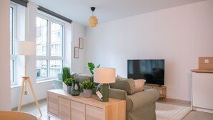 A modern living room with a sofa, TV, and a wooden cabinet with plants. - Appartement, le Petit Cocon (Liege)