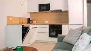 A compact kitchen with white cabinets, a microwave, an oven, and a dishwasher. - Appartement, le Petit Cocon (Liege)