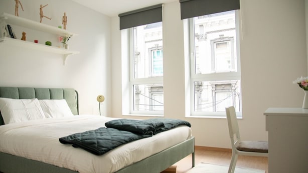 A bedroom with a bed, a chair, a desk, and a window with a view of buildings. - Appartement, le Petit Cocon (Liege)