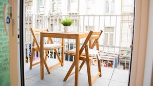 A balcony with a wooden table and chairs, a potted plant, and a view of buildings. - Appartement, le Petit Cocon (Liege)