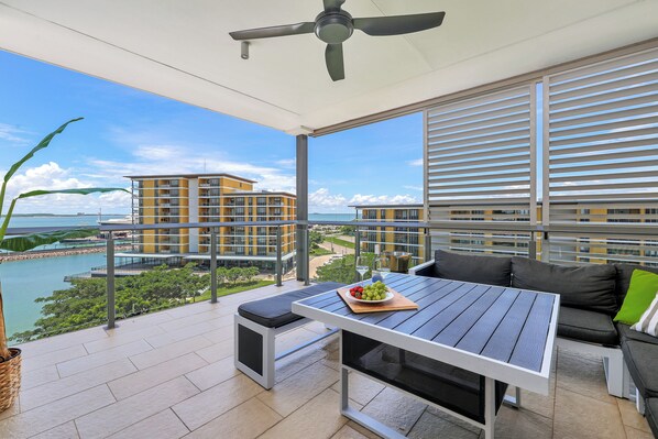 A balcony with a table, seating, and a view of a body of water and buildings.