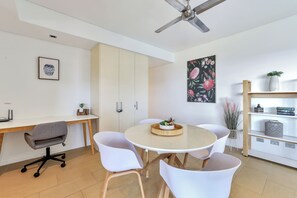 A modern room with a round table, white chairs, a desk with a computer, a ceiling fan, and a bookshelf.