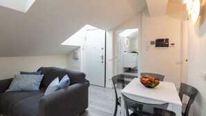 A modern living room with a grey sofa, a glass dining table with a fruit bowl, and a skylight above. - notaMi - Bright Attic M4 - 2 Bedrooms (Milan)